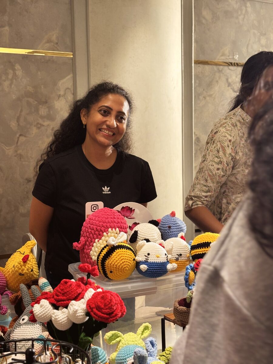 A smiling vendor beside her crochet toys and flowers